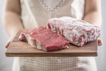 Female cook holding wooden board of raw and frozen beef  meat
