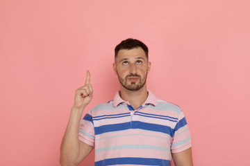 Cheerful bearded man pointing up with finger, over pink background