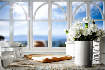 Fototapeta na wymiar White wooden desk in kitchen and blurred background of window and summer landscape of sun and sea 