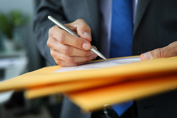 Male clerk in suit and tie at workplace hold in hands silver pen filling out application form