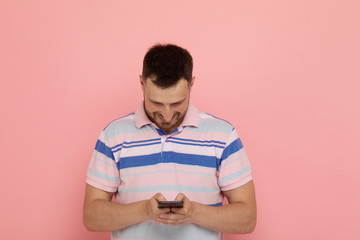 Portrait of a happy young man using mobile phone isolated over pink background.