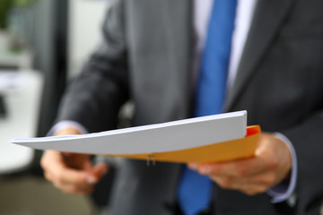 Clerk hand in suit and tie holding yellow envelope containing batch of important papers