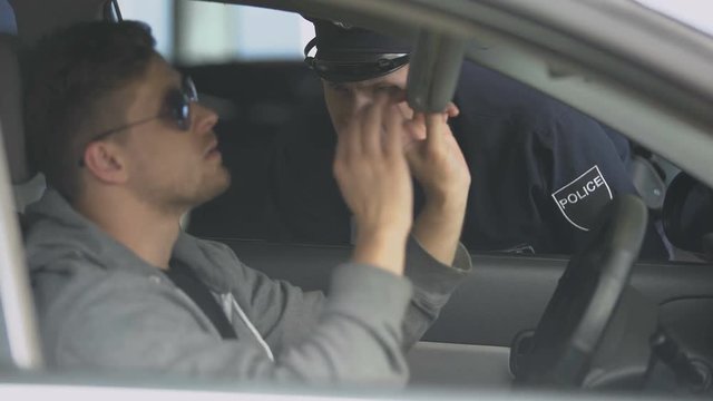 Serious policeman checking male drivers license after exceeding speed limit