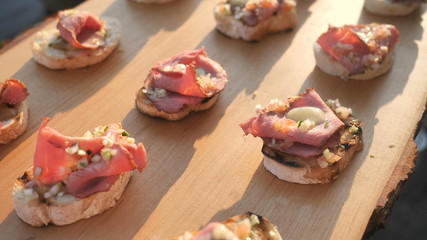 Delicious savory ham (jamon, prosciutto crudo, hamon) Italian appetizers, or bruschetta, on slices of toasted baguette, decorated with natural basil, close-up on a wooden board catering service.