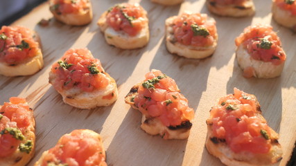 Delicious savory Italian tomato appetizers, or bruschetta, on slices of toasted baguette, decorated with natural basil, close-up on a wooden board.