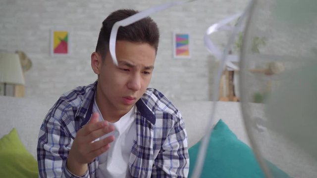 Young asian man saved from the heat sitting in front of a working fan the concept of heat close up