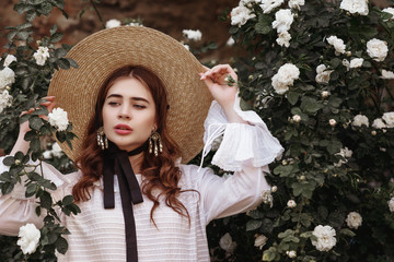 Outdoor close up portrait of young beautiful woman wearing wide brim ribbon tie straw hat, pearl...