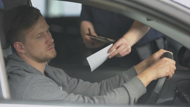 Policeman writing traffic ticket to upset male driver, moving violation, law