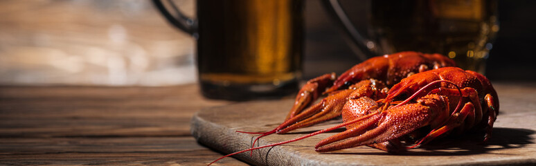 panoramic shot of red lobsters and glasses with beer on wooden surface