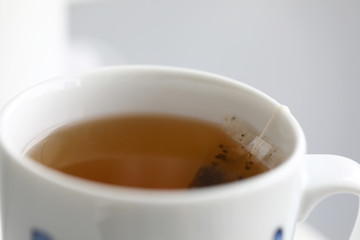 Fresh teabag brewed in white cup hanging out from edge