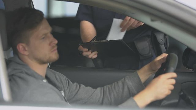 Police officer writing ticket to disappointed male driver, traffic rules brake