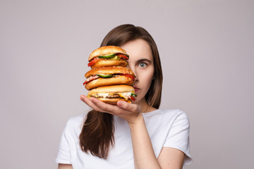 Studio portrait of young brunette woman in white t-shirt holding enormous burgers on her hand...
