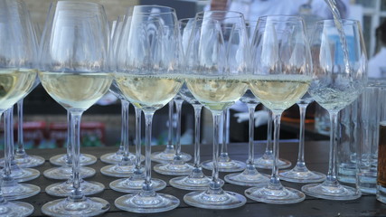 Background of a large number of glasses waiter pours white Italian wine from a traditional grape variety, collected and made by the farmer for craft winemaking