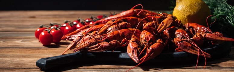 panoramic shot of red lobsters, dill, lemon and tomatoes on wooden surface
