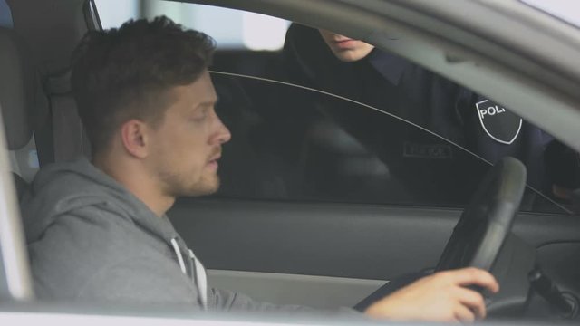 Policeman checking nervous male drivers documents, searching for wanted criminal