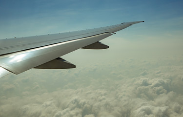 Wing of plane over white clouds. Airplane flying on blue sky. Scenic view from airplane window. Commercial airline flight. Plane wing above clouds. Flight mechanics concept. International flight.