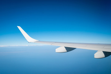 Wing of plane over white clouds. Airplane flying on blue sky. Scenic view from airplane window. Commercial airline flight. Plane wing above clouds. Flight mechanics concept. International flight.