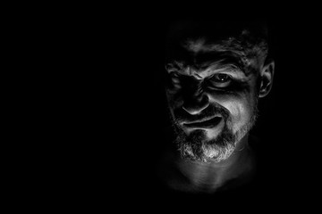  Face with a bearded man grimace against a dark background with sharp shadows. Comedic, fabulous villain or negative character conception with copy space.