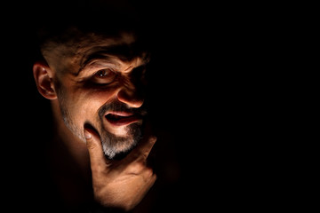  Face with a bearded man grimace against a dark background with sharp shadows. Comedic, fabulous villain or negative character conception with copy space.