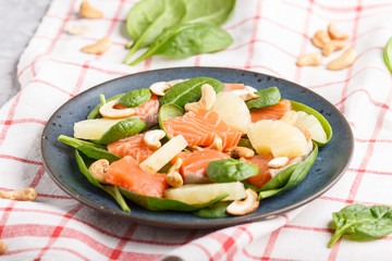 Fresh salmon with pineapple, spinach and cashew in blue ceramic plate on a gray concrete background.