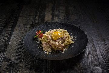 Super tasty bolognese carbonara pasta on a black plates onto dark wooden table. Menu for restaurant
