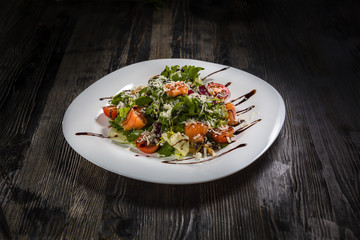 Low key restaurant menu food photo. Delicious fresh salad in white plate on a dark rustic wooden background