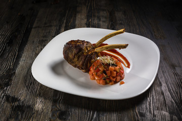 Low key restaurant menu food photo. Delicious fresh ribs with salad in white plate on a dark rustic wooden background