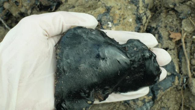 Toxic tar asphalt chemical in glove hand detail. Former dump waste, effects nature from contaminated soil and water with chemicals and oil, black bitumen refined synthetic material close-up