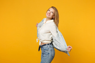 Obraz premium Portrait of cheerful smiling pretty young woman in denim casual clothes standing, looking up isolated on bright yellow orange wall background in studio. People lifestyle concept. Mock up copy space.