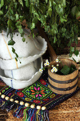 Two hats for the sauna, next to a wooden ladle and fresh birch sauna brooms