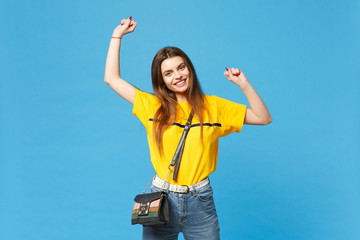 Portrait of smiling young woman in vivid casual clothes with cross body bag clenching fists like winner looking camera isolated on bright blue background. People lifestyle concept. Mock up copy space.
