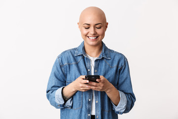 Happy bald woman posing isolated over white wall background using mobile phone.