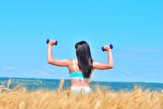 Sporty young woman doing exercise with dumbbells outdoors in a wheat field