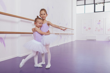 Happy cute little ballerinas having fun at dancing school, hugging, smiling joyfully to the camera,...