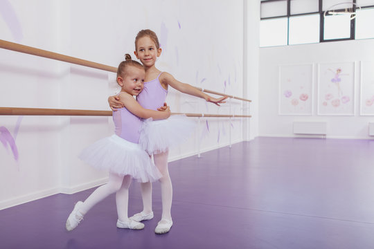 Happy cute little ballerinas having fun at dancing school, hugging, smiling joyfully to the camera, copy space. Adorable little sisters embracing at ballet studio