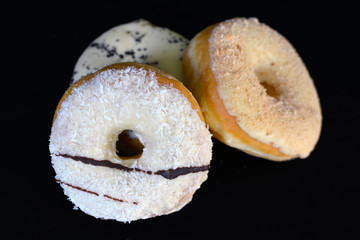 Three delicious donuts glazed with white chocolate and crumble and coconut sprinkles as topping on black 