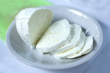 Cut of mozzarella on the white plate, traditional italian cheese