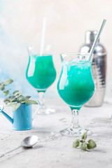Colorful summer cocktail Blue Hawaii or iced blue lagoon alcohol drink with mint on light stone background