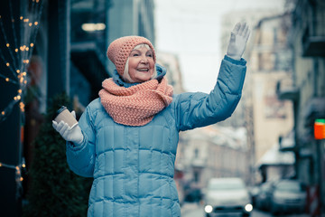 Aged woman in warm clothes waving and smiling