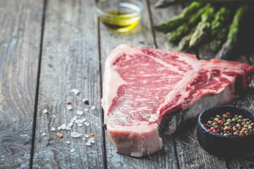 Raw T-bone Steak with fresh herbs and oil on dark wooden background