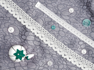 Lace, needle case, tape measure, buttons on a background of gray fabric. Concept sewing still life