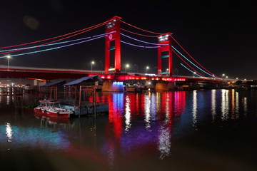 Palembang's Ampera bridge is photographed at night, with natural lighting and slow speed photography techniques.