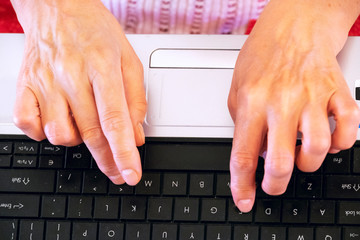 Hands of an old caucasian woman are typing on a laptop keyboard. View from above
