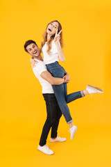 Full length portrait of excited couple in basic t-shirts standing together while man picking up and hugging pretty woman