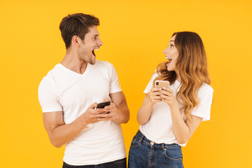 Portrait of attractive couple man and woman in basic t-shirts looking at each other while holding smartphones
