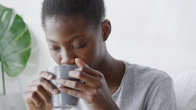 Medium shot of young black woman waking up in the morning and having cup of refreshing hot coffee or tea