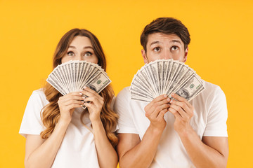 Portrait of joyful couple man and woman in basic t-shirts rejoicing while holding bunch of money cash