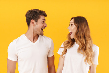 Portrait of amazed couple man and woman in basic t-shirts wondering with open mouthes while looking at each other