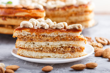 Piece of homemade cake with caramel cream and nuts on a gray concrete  background, side view.