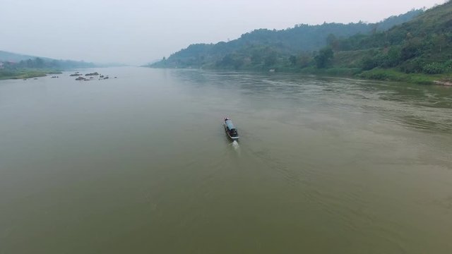 A wide shot of a boat carrying passengers sailing on a river bounded on one side by hills